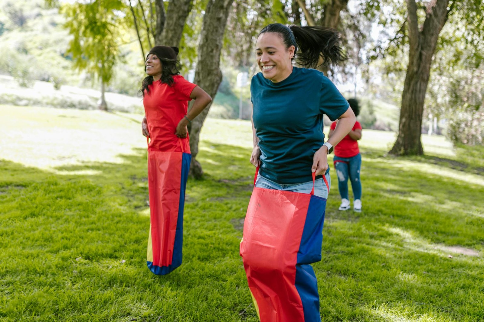 Adults participating in a fun sack race competition outdoors in a park setting, showcasing team spirit and enjoyment.